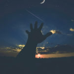 Human hand connecting to sky, stars, crescent moon and sun above Earth's horizon